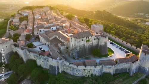 Aerial view of a historic fortified town on a hill at sunset. Fortified walls encircle buildings