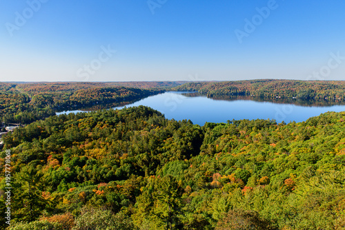 Quadro su tela Panoramic view of winding lake nestled among rolling hills covered in autumn fol