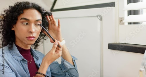 Non-binary person reaching for eyeshadow brush dipping into palette, blending into crease at vanity