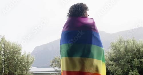 Non-binary person spotting mountain view adjusting rainbow flag, unfolding to show pride on terrace