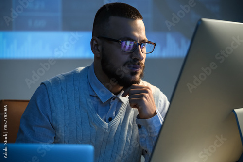 Foto Thoughtful male trader with eyeglasses working in dark office