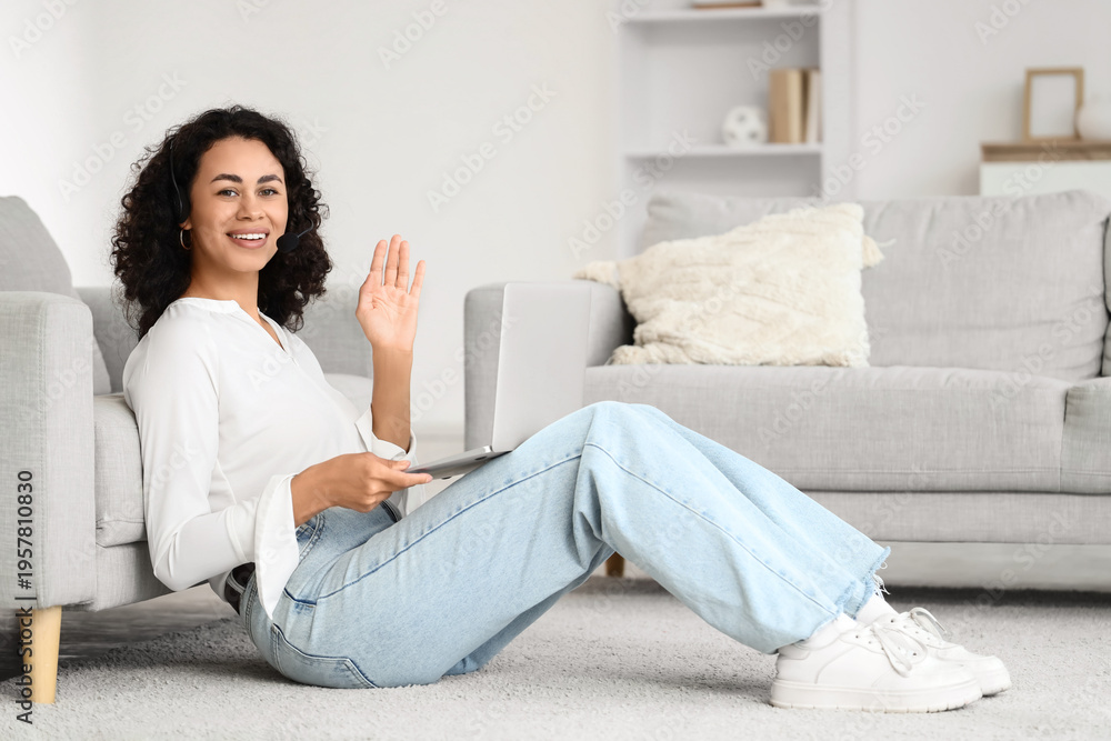 Fototapeta premium Female African-American online business consultant with laptop waving hand at home