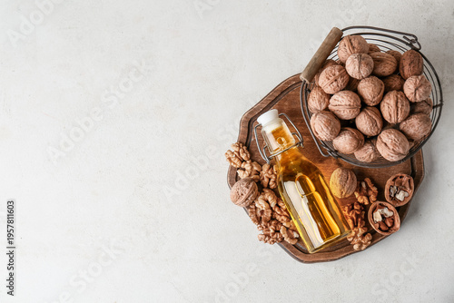 Bottle of fresh walnut oil and basket with nuts on white background