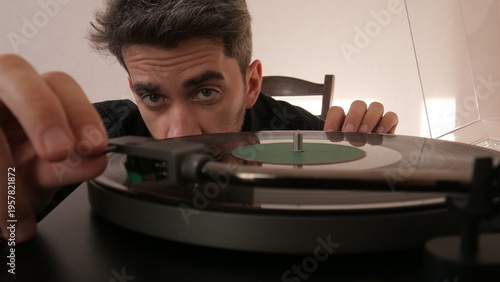 Man carefully dropping the tonearm needle onto a spinning vinyl record, preparing to listen to analog music from the turntable, showcasing a passion for vintage audio