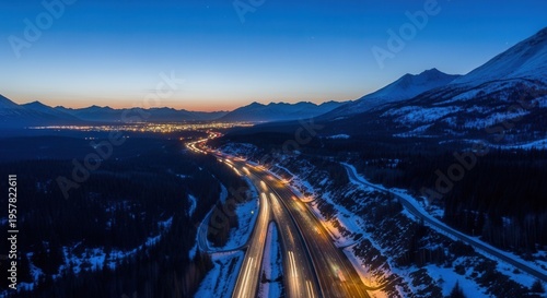 Illuminated Highway Leads to Distant Cityscape Amidst Snowy Mountains At Twilight
