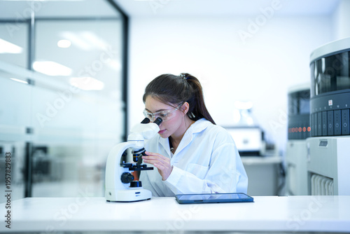 Cuadro en lienzo Focused female scientist using a microscope and digital tablet to analyze research data in a modern sterile laboratory