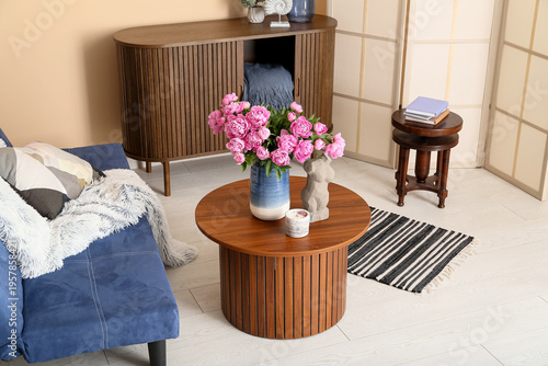 Vase of pink peonies on coffee table, couch and dresser near beige wall