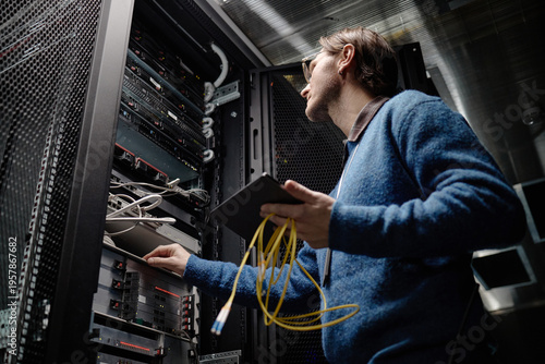 Quadro su tela Middle aged Caucasian man working in server room holding tablet and yellow netwo