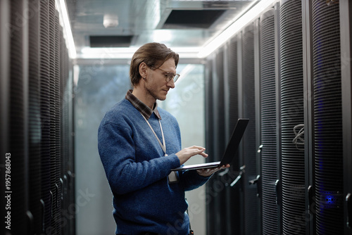 фотографія Caucasian middle aged man working on laptop inside server room, standing between