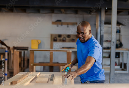 African American man in bright blue Tshirt measuring wood with tape measure in workshop, copy space