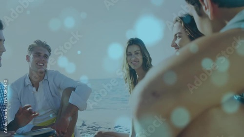 Vertical video: Camera pulling back group chatting on sand while playing guitar drum, bokeh overlay