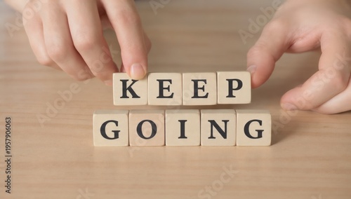 Hands arranging wooden blocks spelling motivational message Keep Going