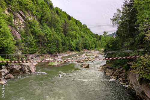 Suspension bridge over mountain river in Yaremche forest valley