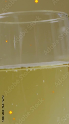 Vertical video: Camera revealing glass while bubbles rising and amber sparks drifting for drink ad