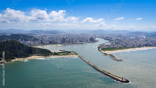 Aerial view of the entrance to Itajaí Port with the city skyline and coastline under a clear blue sky.