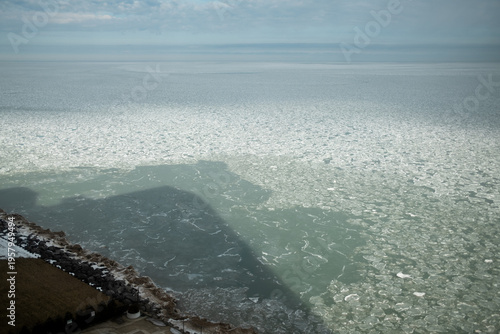 Aerial View of Frozen Sea and Ice Floes Along a Winter Shoreline With Building Shadow