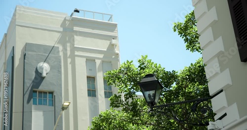 Camera tilting upward on street, revealing sky, breeze causing leafy tree swaying by black lamp