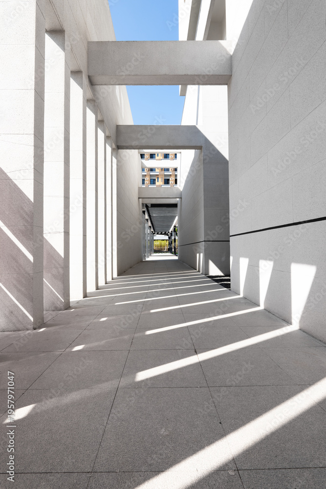 Naklejka premium Modern architectural corridor with intersecting light and shadow patterns in a long passageway