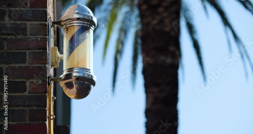 Internal motor is turning barber pole on brick wall while sunlight is glinting on chrome caps