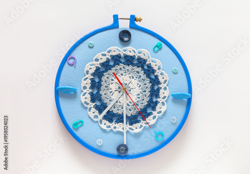 Time for craft, knit and crocheting. Handmade wall clock with knitting and sewing accessories instead of numbers and lace doily decorate dial in blue hoop. Concept of hobbies, leisure, and needlework