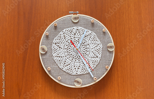 Time for crafts and crochet. Handmade wall clock with buttons and beads instead of numbers and lace doily to decorate the dial on wooden background. Hobbies and relaxation through needlework