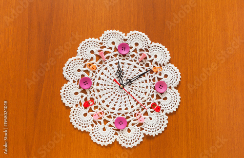Time for craft and crochet. Handmade clock with knitting and sewing accessories instead of numbers and beautiful lace doily to decorate dial on wooden background. Hobby, leisure and needlework concept