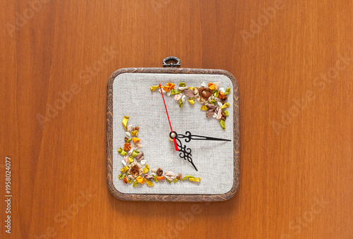 Time for crafts and embroidery. Handmade wall clock with satin ribbon embroidery on linen canvas to decorate square dial in a hoop. Hobbies and relaxation through embroidery concept