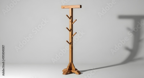 A wooden coat rack with multiple hooks stands alone in a room with a shadow on the wall behind