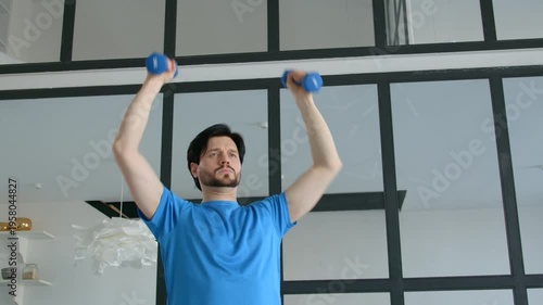 Determined handsome sporty fit man practicing dumbbell standing shoulder press, improving strength in chest, shoulders, deltoids, and triceps during indoor sports training