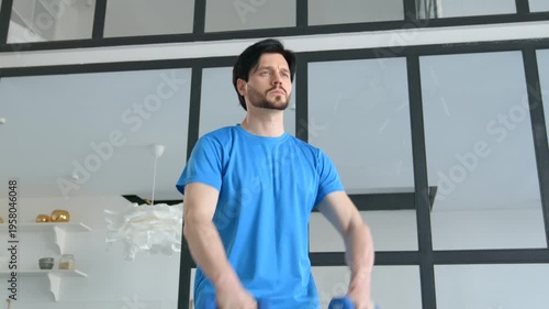 Active sporty muscular build man practicing dumbbell front raise to lateral raise exercise, strengthening middle deltoids and anterior deltoids of shoulders indoors.