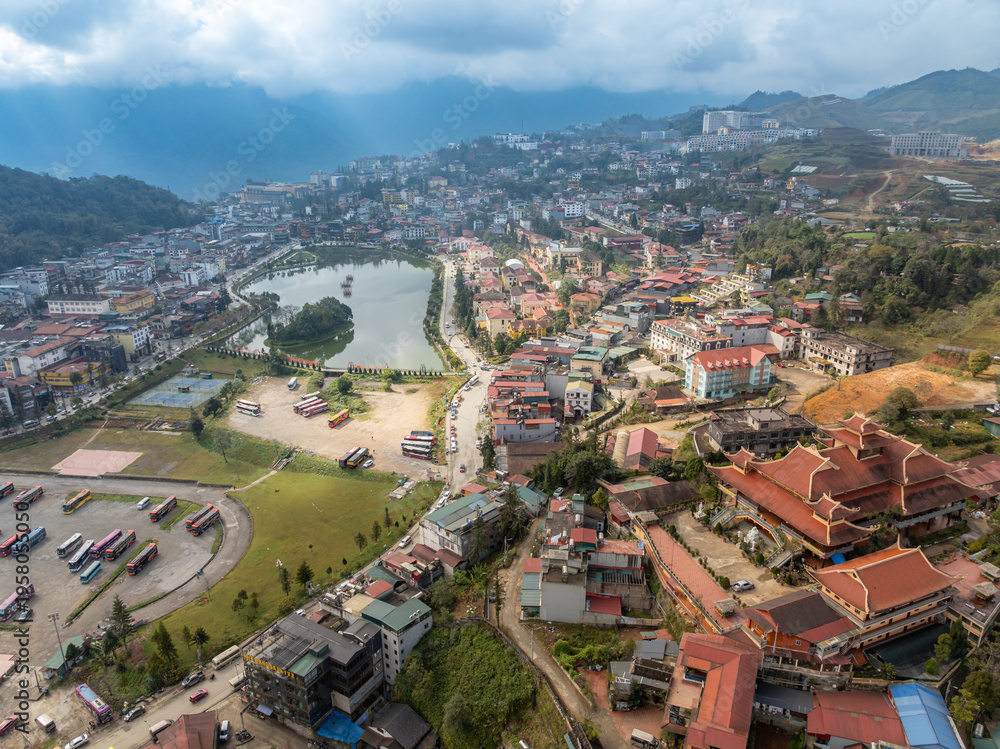 Fototapeta premium Aerial view of Sapa, Vietnam, showcasing the town's architecture, lake, and surrounding mountains. Tourists visit to experience the culture and scenery.