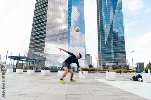Cuadro en lienzo Young man doing freestyle soccer tricks with a ball outdoors, with modern skyscr