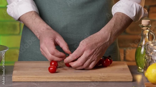 A male chef picks tomatoes from a vine to prepare a salad.