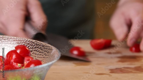 A cook transfers sliced tomatoes into a bowl to prepare a salad. Close-up.