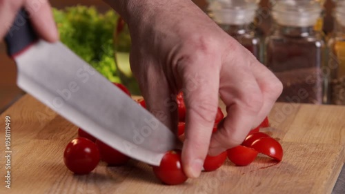 A male chef cuts tomatoes in half to prepare a salad.