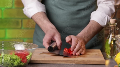 A male chef transfers chopped tomatoes into a bowl to prepare a salad.