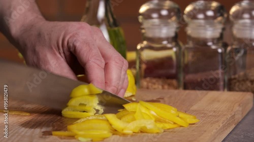 A male chef slices yellow bell pepper with a knife on a cutting board to prepare a salad.