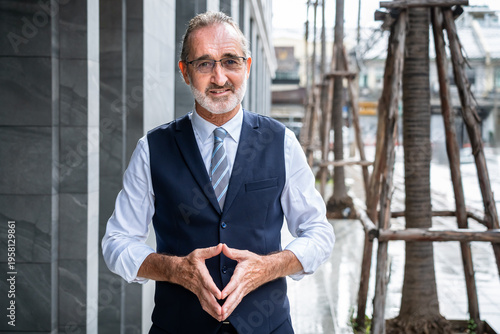 Confident mature Caucasian businessman standing outdoors with hands forming triangle gesture wearing formal suit in modern city, looking at camera