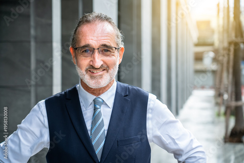 Smiling mature Caucasian businessman standing with hands on hips confident posture wearing eyeglasses formal business attire outdoor, looking at camera