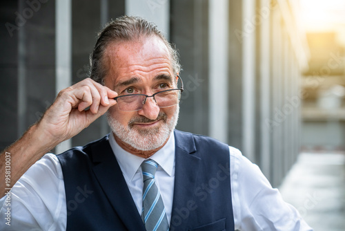 Smiling mature Caucasian businessman adjusting glasses with hand close up portrait wearing formal suit outdoors in modern city