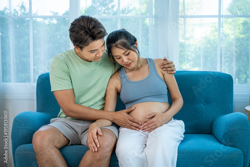 Asian expecting parents sharing tender moment, touching baby belly at home