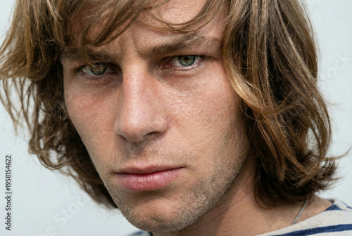 Young man with medium-length brown hair looks directly at camera. His expression is serious and focused