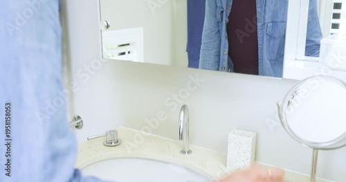 non-binary person applying eyeliner pencil on eyes at bathroom mirror