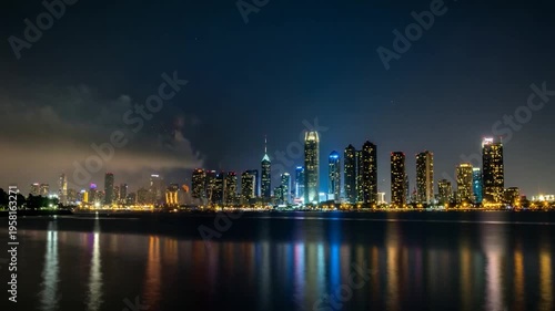 Vibrant fireworks burst over a city skyline at night, reflected in calm water