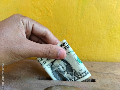 Person donating US dollar banknote into a charity box, concept of generosity, philanthropy, and financial support for social causes.