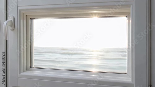 View of the ocean through a white window frame with sunlight reflecting on the water.