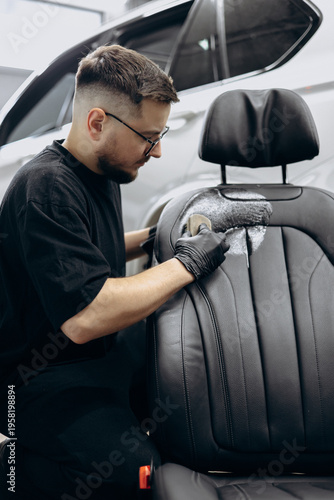 Man cleaning car seat with brush and soap at car detailing service
