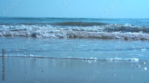 Blue waves crash against the sandy coast under a summer sky as the ocean tide meets the shore in this scenic nature landscape