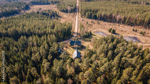 Aerial view of a rural landscape featuring a small house surrounded by dense forest and a dirt road leading through the trees in a tranquil natural setting