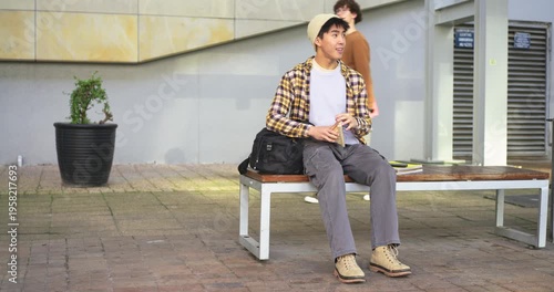 Asian man opening backpack, pulling sandwich, taking lunch on courtyard bench, glancing at passerby